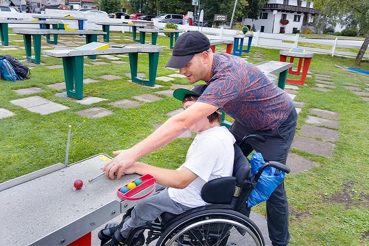 Ein Mann hilft einen Jugendlichen im Rollstuhl beim Tischgolf.