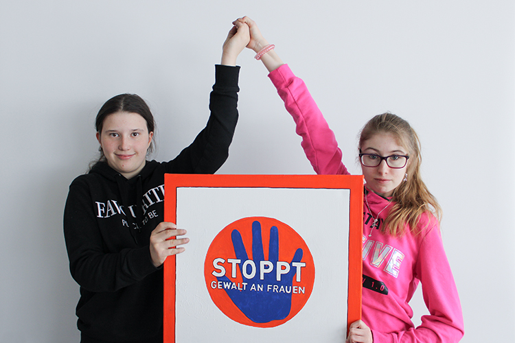 Zwei juneg Frauen halten ein Bild mit der Aufschrift "Stoppt Gewalt an Frauen"